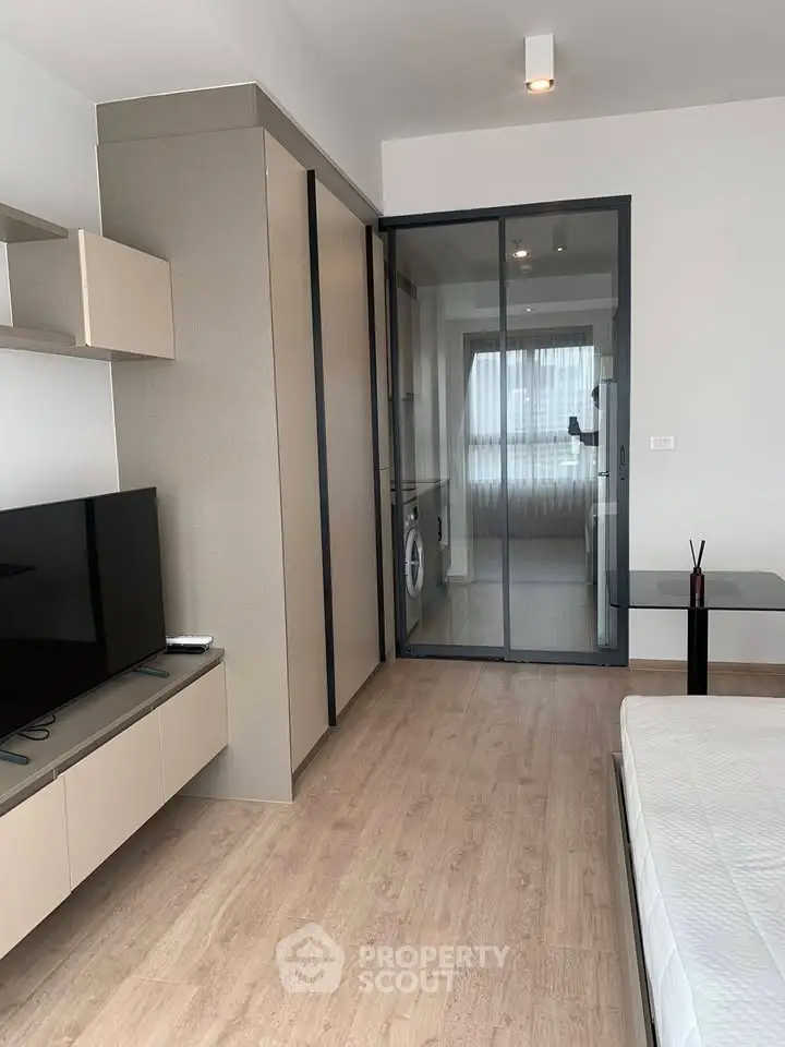 Modern studio apartment with sleek design and glass partition, featuring a cozy living area and natural light.