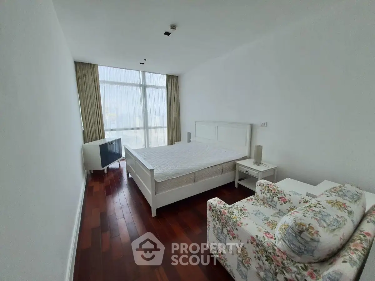 Spacious bedroom with wooden flooring and large window offering natural light.