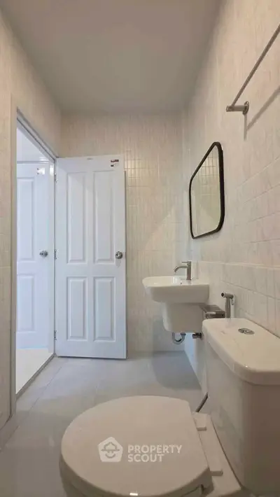 Modern bathroom with sleek fixtures and neutral tiles, featuring a toilet, sink, and mirror.