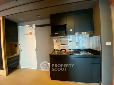 Modern compact kitchen with sleek black cabinetry and stainless steel appliances in a stylish apartment.