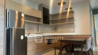 Modern kitchen with sleek cabinets and dining area, featuring contemporary lighting and stainless steel fridge.