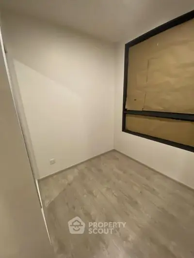 Minimalist small room with wooden flooring and large window, perfect for a cozy bedroom or study.
