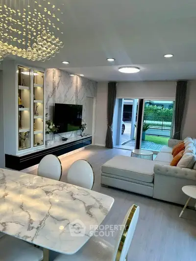 Luxurious living room with elegant marble dining table and spacious seating area, opening to a lush garden view.
