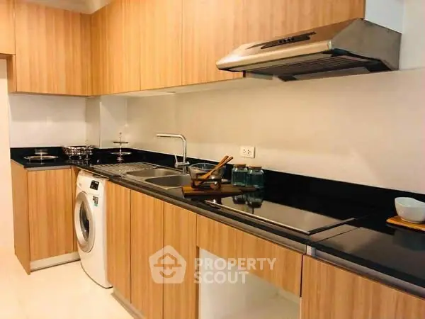 Modern kitchen with wooden cabinets, washing machine, and sleek black countertops.