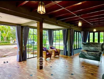 Spacious living room with large windows and garden view, featuring wooden ceiling and tiled floor.
