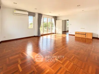 Spacious sunlit living room with wooden flooring and large windows in modern apartment.