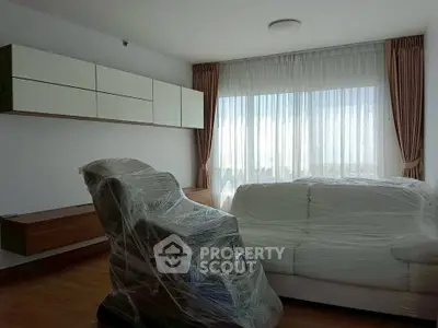 Spacious living room with modern furniture wrapped for protection, featuring large windows and elegant curtains.