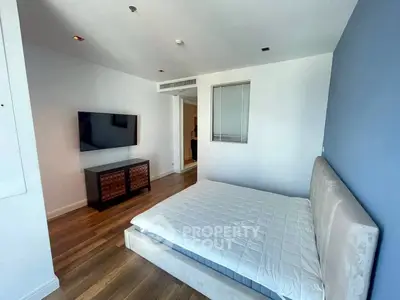 Modern bedroom with sleek design and wall-mounted TV, featuring hardwood floors and minimalist decor.