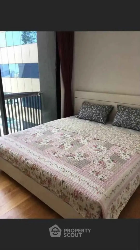 Cozy bedroom with floral bedding and large window offering natural light in modern apartment.