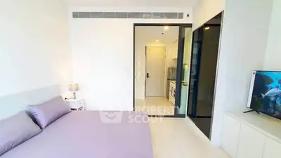 Modern bedroom with sleek design and open view to kitchen area, featuring minimalist decor and natural light.