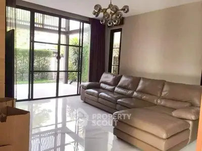 Spacious living room with modern leather sofa and large windows opening to garden view.