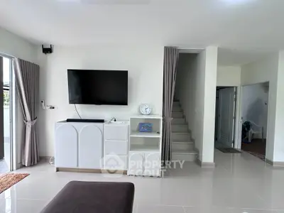 Modern living room with sleek TV setup and elegant staircase in a bright, open space.