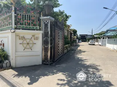 Charming residential entrance with decorative gate and lush greenery in a serene neighborhood setting.