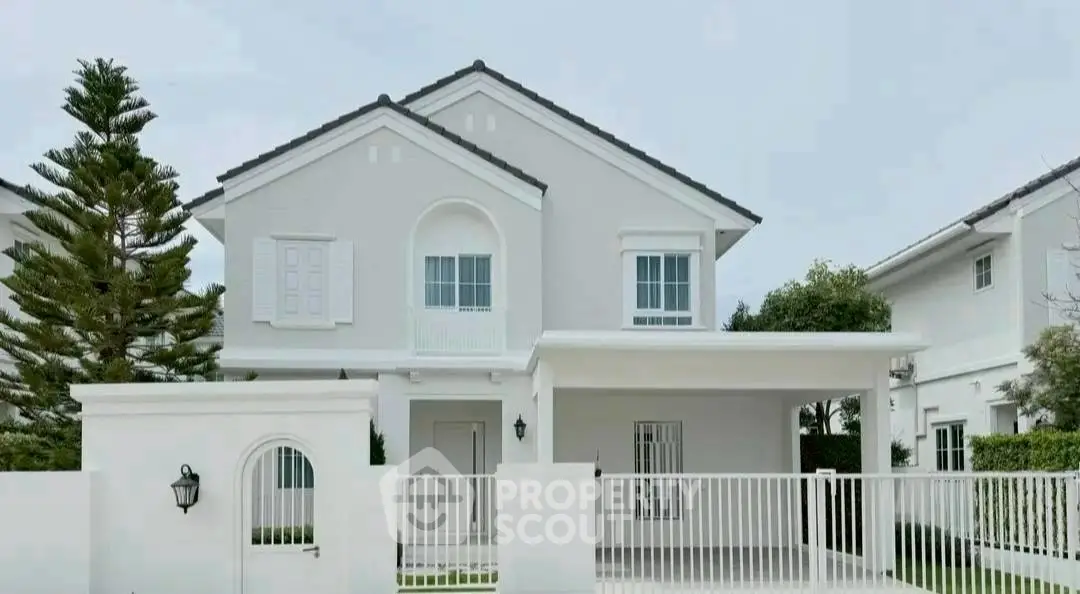 Charming two-story white house with gated entrance and lush greenery.