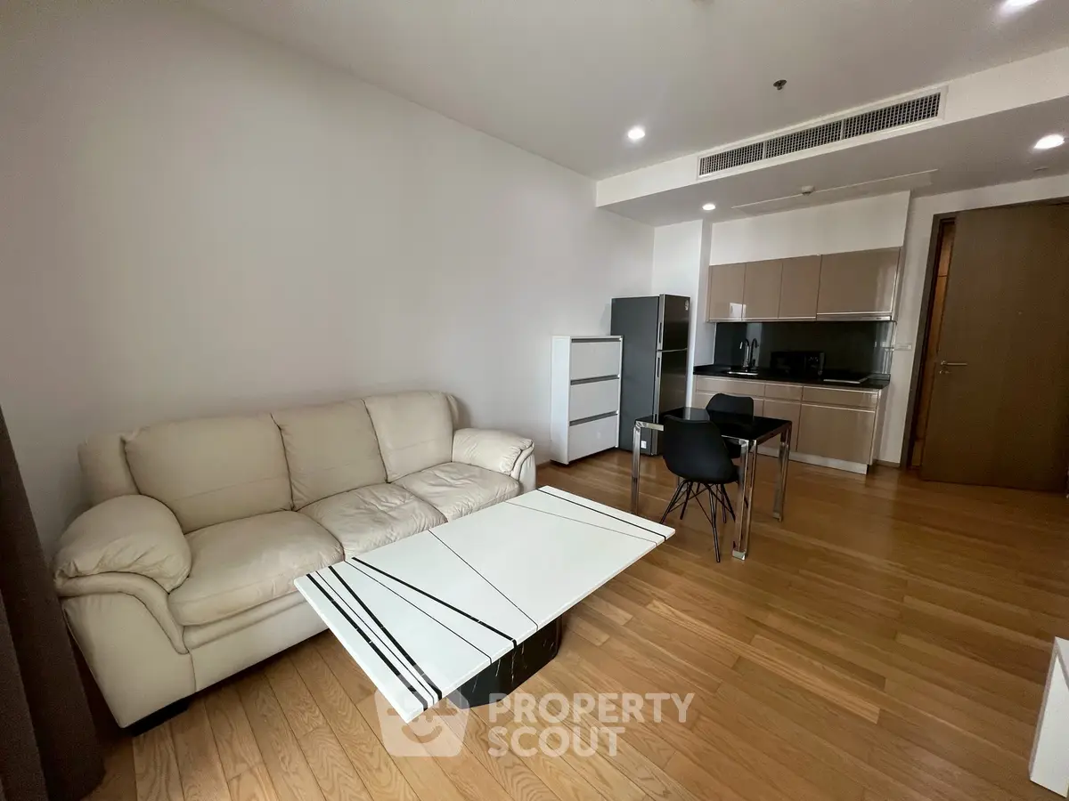 Modern living room with open kitchen, featuring sleek furniture and wooden flooring.