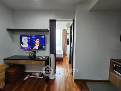 Modern apartment interior with wooden flooring, TV, and view into bedroom