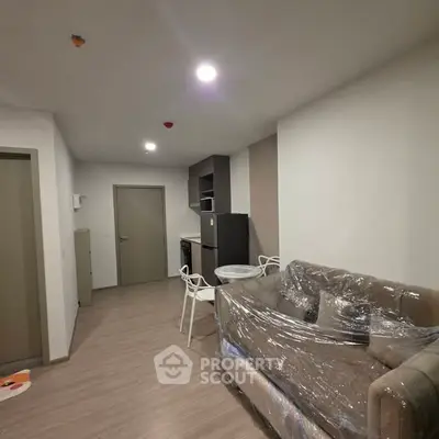 Modern apartment interior with compact kitchen and cozy living area, featuring a wrapped sofa and dining set.