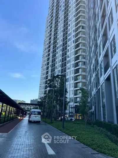 Modern high-rise apartment building with lush landscaping and paved walkway.