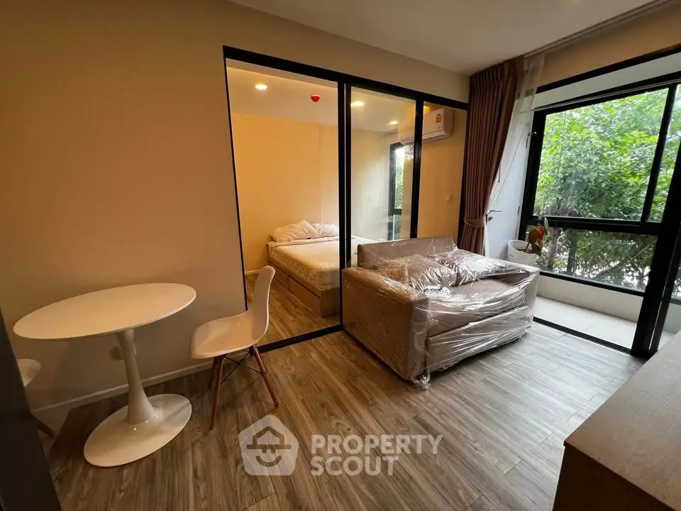 Modern studio apartment with cozy living area and bedroom, featuring large windows and stylish furniture.