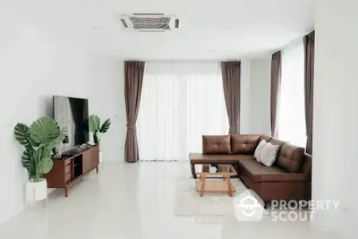 Modern living room with sleek brown sofa and large TV in bright airy space