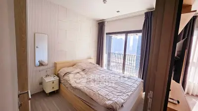 Modern bedroom with large window and city view, featuring cozy bed and stylish decor.