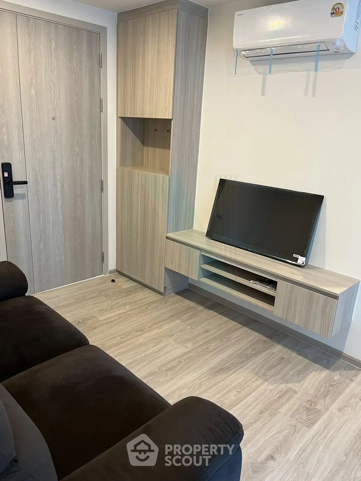 Modern living room with sleek wooden flooring, mounted TV, and air conditioning unit.