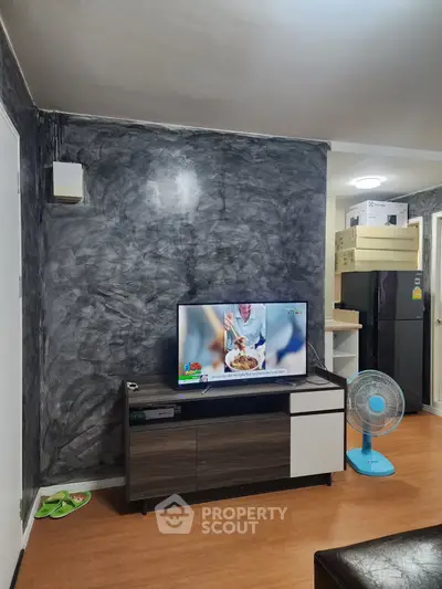 Modern living room with stylish TV stand and textured wall, featuring a sleek refrigerator and fan for comfort.