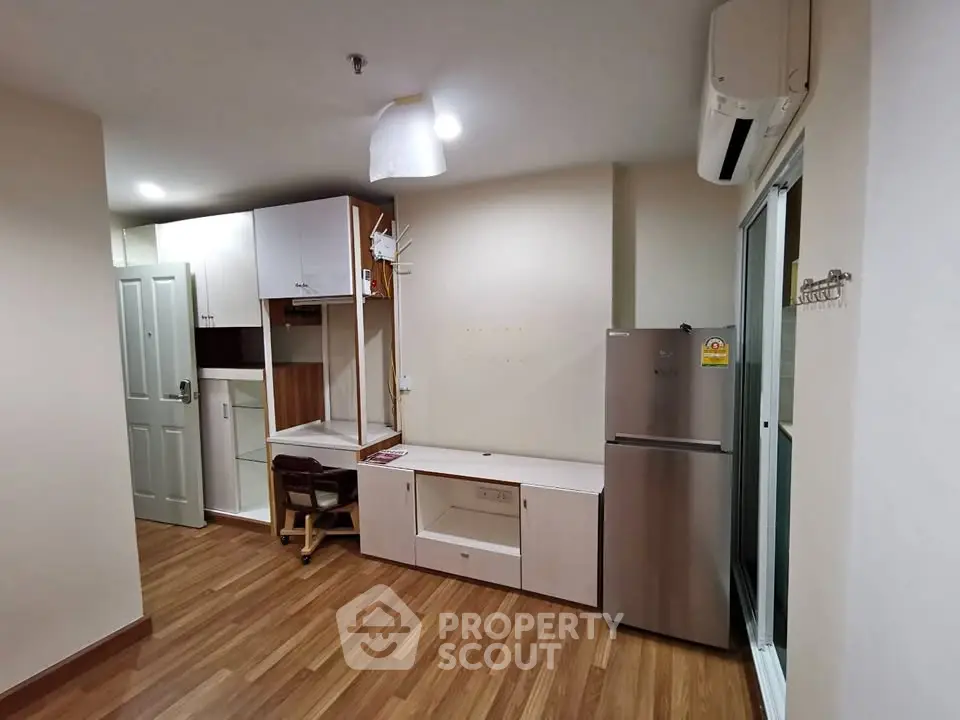 Modern apartment interior with wooden flooring and built-in furniture, featuring a fridge and air conditioning.