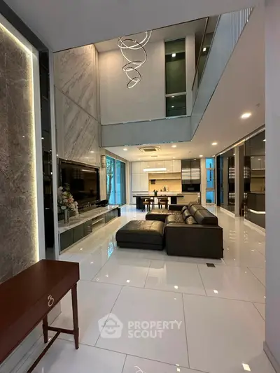 Luxurious open-plan living room with modern kitchen and high ceilings, featuring elegant decor and ample natural light.