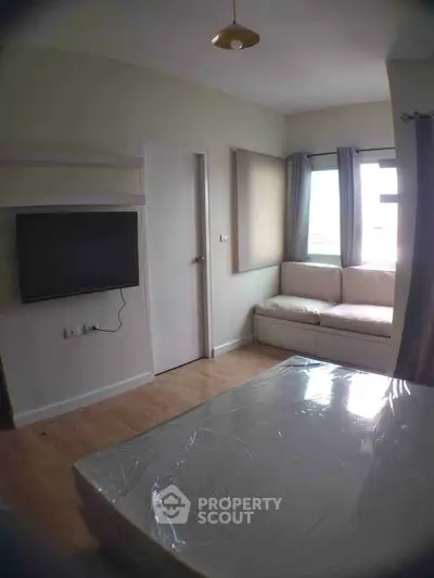 Cozy bedroom with natural light, featuring a wall-mounted TV and a comfortable seating area by the window.