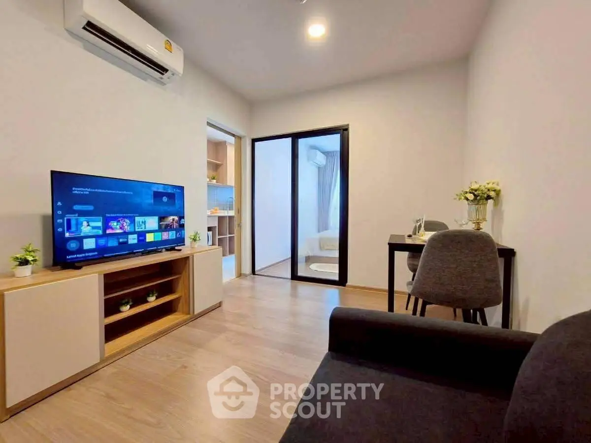 Modern living room with sleek furniture and open layout, featuring a flat-screen TV and air conditioning.