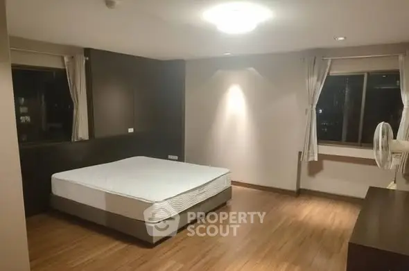 Spacious bedroom with wooden flooring and large windows for natural light.