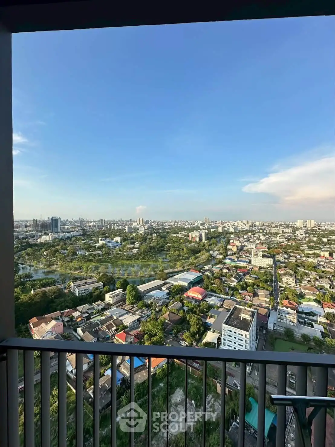 Stunning high-rise balcony view overlooking a vibrant cityscape with lush greenery and clear blue skies.