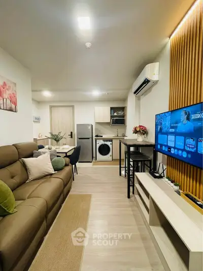 Modern living room with open kitchen, featuring a cozy sofa, flat-screen TV, and stylish decor.