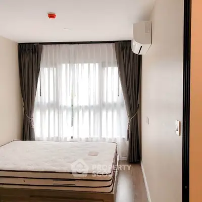 Modern bedroom with large window and air conditioning unit, featuring elegant curtains and a comfortable mattress.