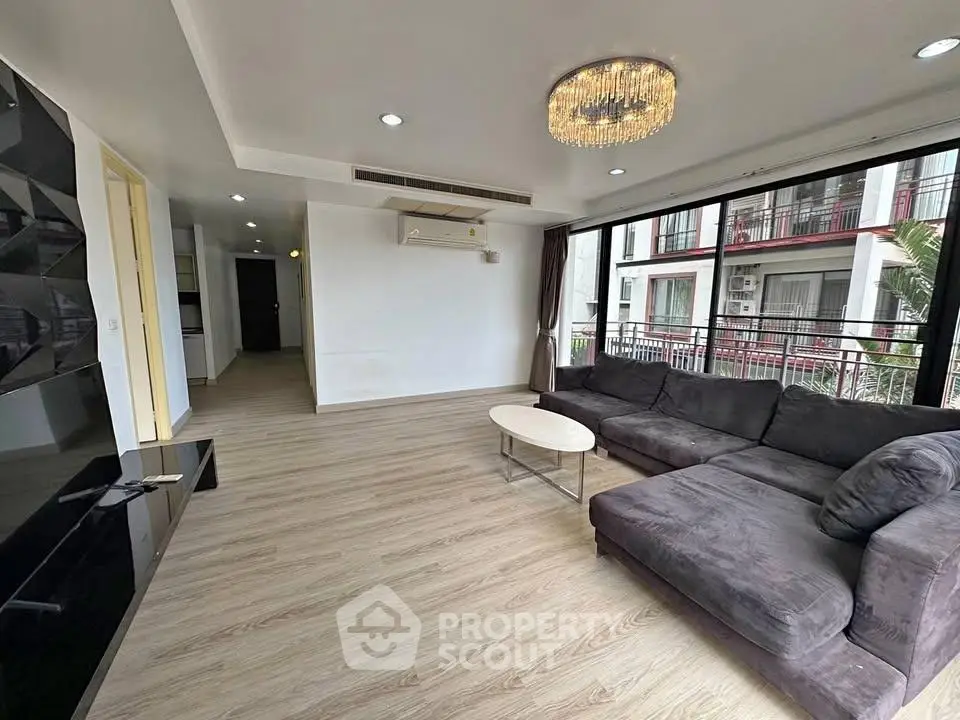 Spacious modern living room with large windows and elegant chandelier in a stylish apartment.