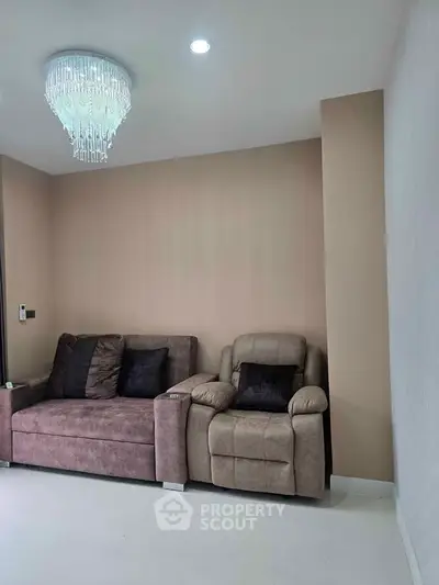 Elegant living room with plush sofa and armchair under a modern chandelier, perfect for cozy relaxation.