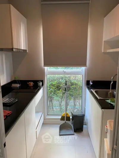 Modern kitchen with sleek white cabinetry and black countertops, featuring a large window with a serene garden view, perfect for culinary enthusiasts.