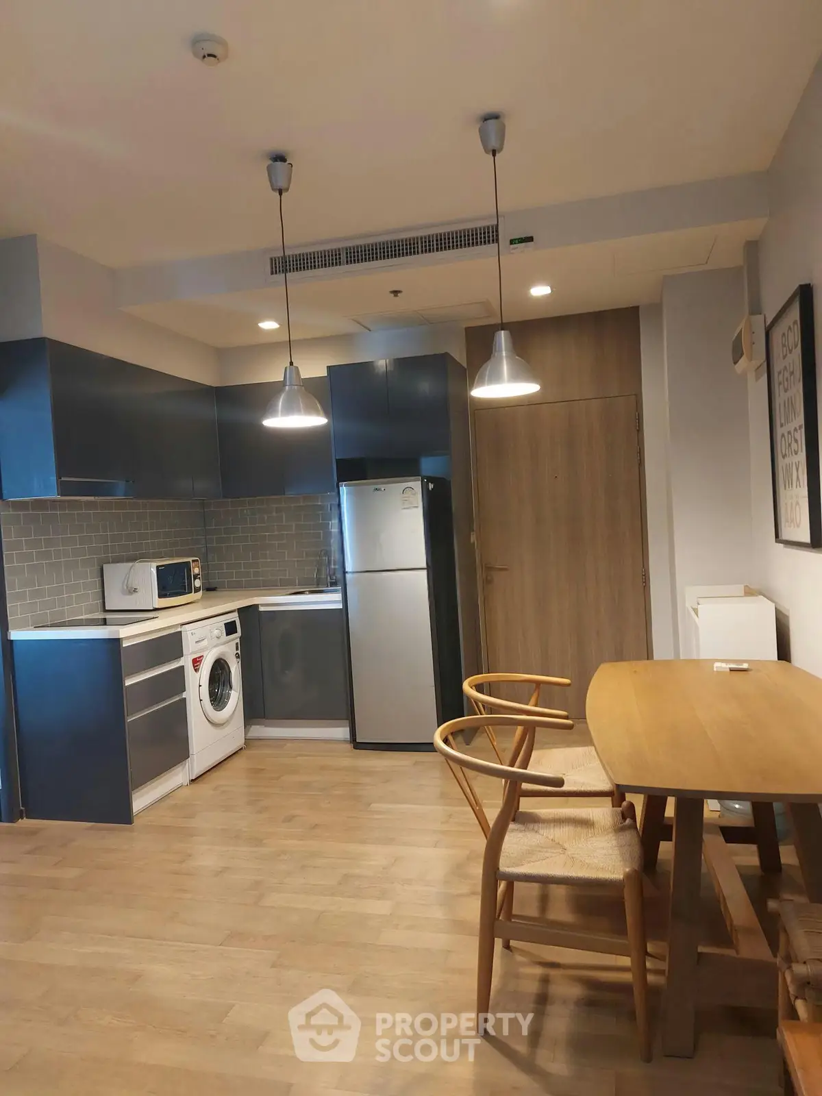Modern kitchen with sleek cabinets, washing machine, and dining area in open layout apartment.