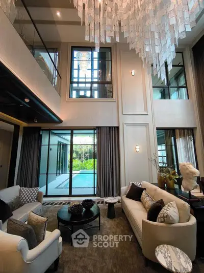 Luxurious living room with high ceilings, elegant chandelier, and pool view in modern home.