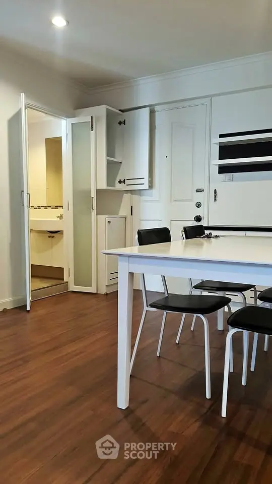 Modern dining area with sleek white table and chairs, adjacent to a compact bathroom.