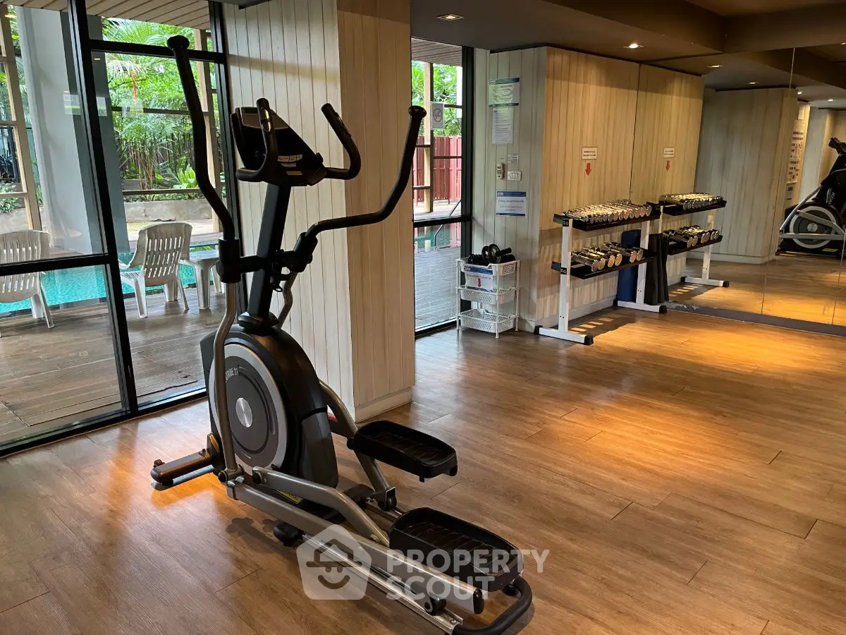 Modern gym with elliptical machine and weights, overlooking a pool area.