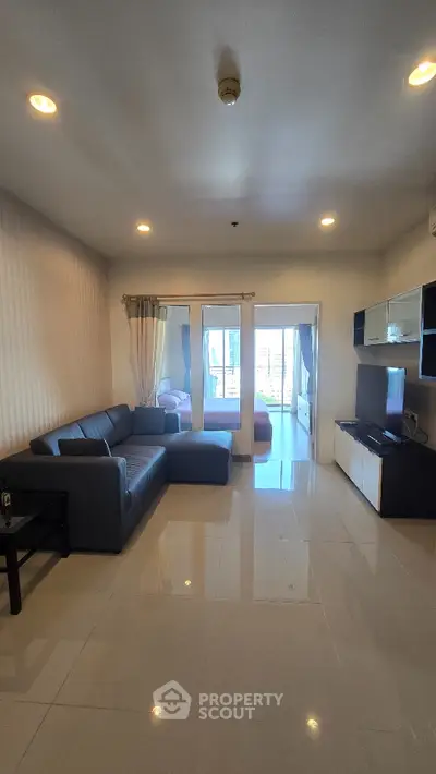 Spacious living room with modern sofa and TV unit, leading to a bright balcony view.