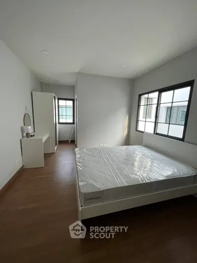 Spacious bedroom with large windows and natural light, featuring a modern bed and sleek wooden flooring.