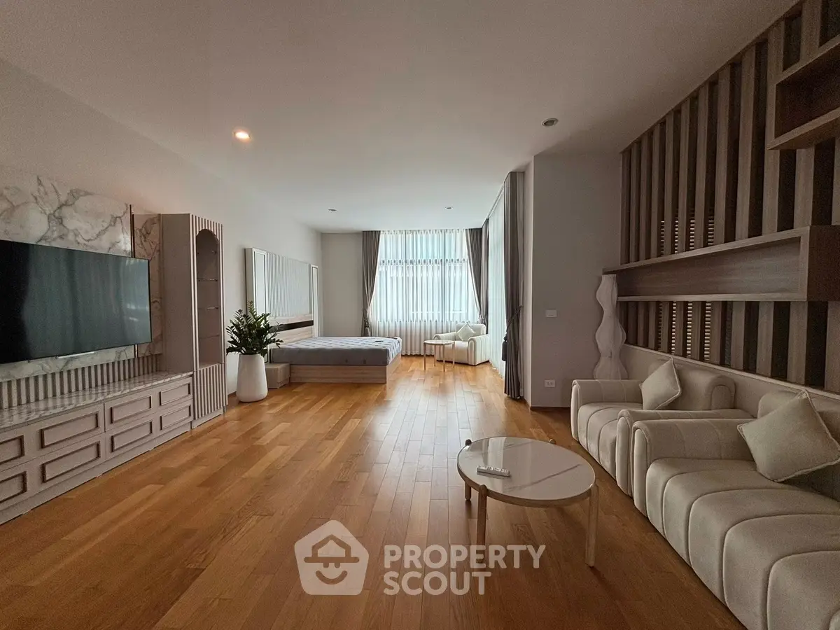 Spacious modern living room with wooden flooring, large TV, and elegant furniture.