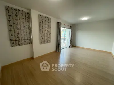 Spacious empty room with wooden flooring and large windows for natural light.