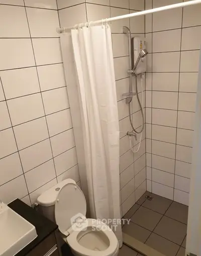 Compact bathroom with shower and toilet, featuring white tiles and modern fixtures.