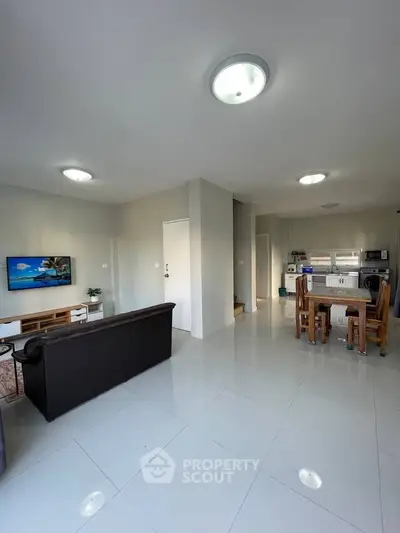 Spacious open-plan living room with modern kitchen and dining area, featuring sleek tile flooring and contemporary lighting.
