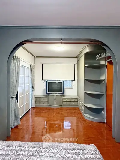 Spacious living room with vintage TV and built-in shelves, featuring elegant archway and polished wooden floors.