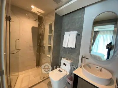 Modern bathroom with glass shower, sleek sink, and large mirror in a stylish apartment.